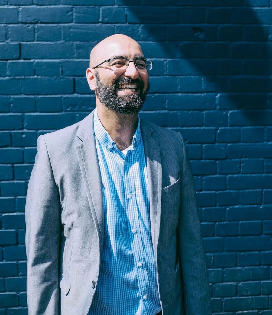Shamash Alidina, smiling, in front of a brick wall
